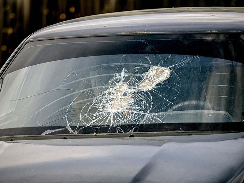 Cracked car windshield from flying debris, illustrating potential glass damage and tips to prevent costly repairs